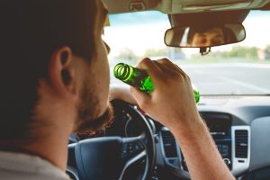 Drunk young man driving a car with a bottle of beer